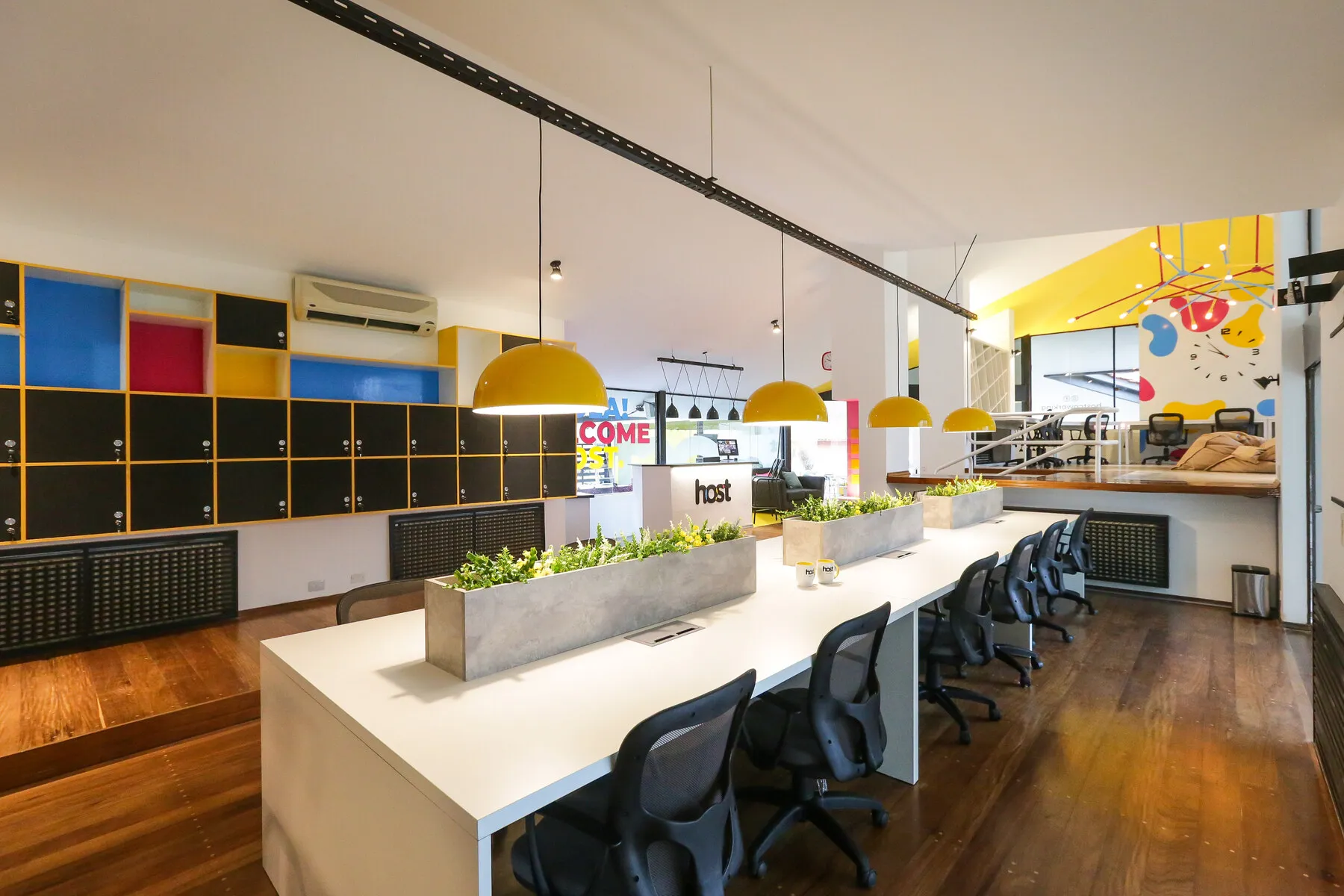 Zona de escritorios compartidos con lámparas amarillas colgantes en Host Coworking