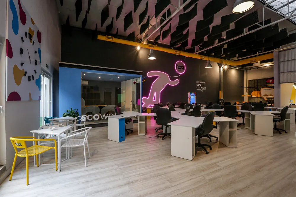 Área de trabajo corporativa junto a la cabina acústica con acento de neón en Host Orfeo