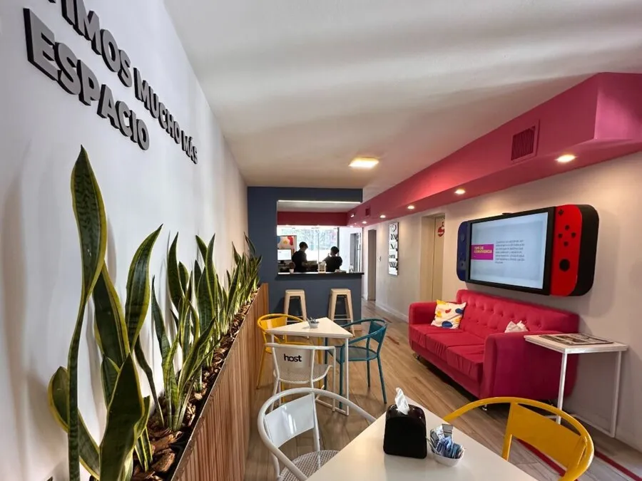 Lounge de Host Orfeo con sillón rojo, pantalla y mensaje Compartimos mucho más que un espacio
